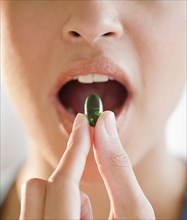 Mixed race woman putting green capsule into mouth