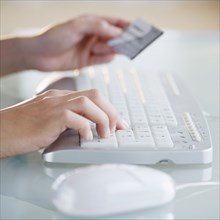 Hands holding credit card while typing on computer keyboard