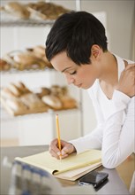 Mixed race woman in bakery writing in notepad