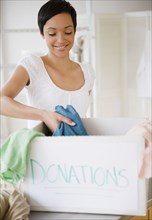 Mixed race woman putting clothing in donation box
