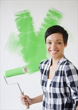 Mixed race woman holding paint roller with green paint