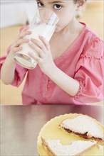 Mixed race girl drinking milk and eating sandwich