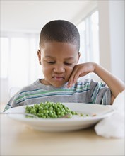 African American grimacing at plate of peas
