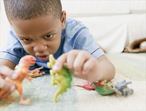 African American boy laying on floor playing with toy dinosaurs