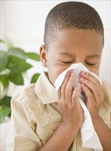 African American boy sneezing into tissue