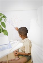 African American boy drawing on wall with crayon