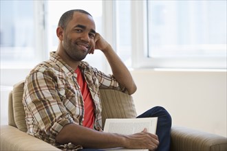 Mixed race man sitting in armchair reading book