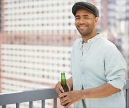 Mixed race man drinking beer near railing
