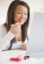 Smiling mixed race teenage girl applying lip gloss in mirror