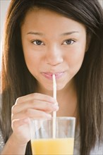 Mixed race teenage girl sipping orange juice with straw