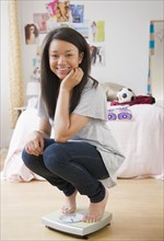 Smiling mixed race teenage girl crouching on scale