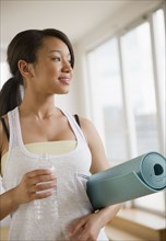 Smiling mixed race teenage girl holding yoga mat and water bottle