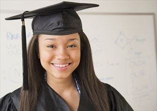 Smiling mixed race teenage girl wearing cap and gown