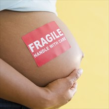 Close up of 'Fragile' sticker on pregnant Black woman's stomach