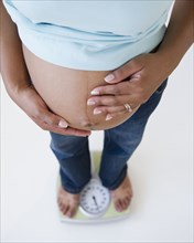Pregnant Black woman holding stomach and standing on scale
