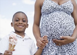 Smiling Black boy holding melting ice cream cone and pregnant mother's hand
