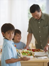 Smiling boy serving salad to family