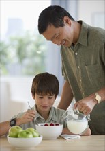 Smiling father pouring milk on son's cereal