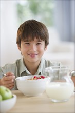 Smiling mixed race boy eating cereal at table