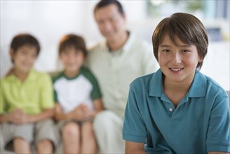 Smiling boy in living room with father and brothers in background