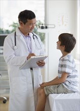 Doctor with medical chart talking to boy in examination room