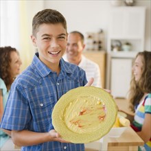 Smiling boy displaying empty plate with family at table in background