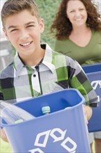 Hispanic boy carrying recycling bin with mother in background
