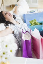 Smiling Hispanic woman sitting on sofa with shopping bags