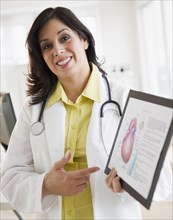 Smiling Hispanic doctor holding up diagram of heart