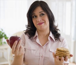 Smiling Hispanic woman choosing between cookies and apple