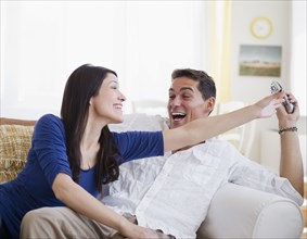 Laughing mixed race man keeping remote control away from wife