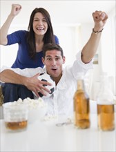 Mixed race couple drinking beer and cheering on soccer match