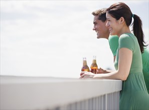 Smiling couple drinking beer on balcony