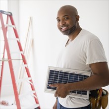 African American construction worker carrying solar panel