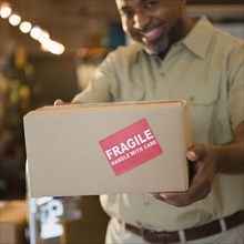 African American deliveryman holding out box with 'fragile' sticker