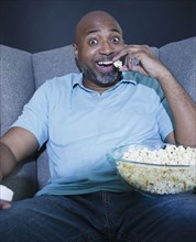 African American man eating popcorn and watching television