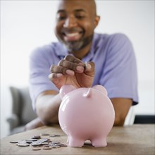 Smiling African American man putting coins in piggy bank