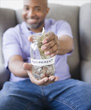 Smiling African American man holding out jar with retirement money