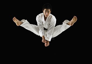 Asian male karate black belt kicking in air