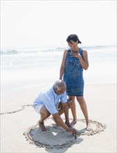 Black man drawing heart on beach for wife