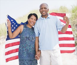 Black couple on beach wrapped in American flag