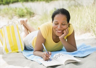 Black woman doing crossword puzzle on beach