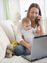 Mother holding baby and using telephone and laptop