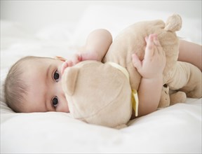Mixed race baby laying on bed with teddy bear