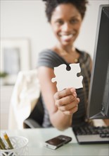 Black businesswoman holding puzzle piece at desk