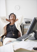 Black businesswoman reclining at desk
