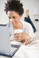 Black woman laying on bed using computer
