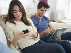 Couple using technology on sofa together