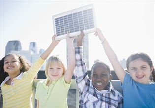 Children on rooftop holding up solar panel
