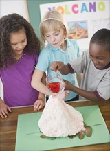 Children watching boy with model volcano